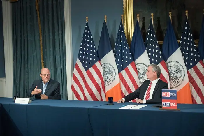United Federation of Teachers president Michael Mulgrew sits toward the left side of a long conference table several feet from Mayor Bill de Blasio at a news conference on September 1st.